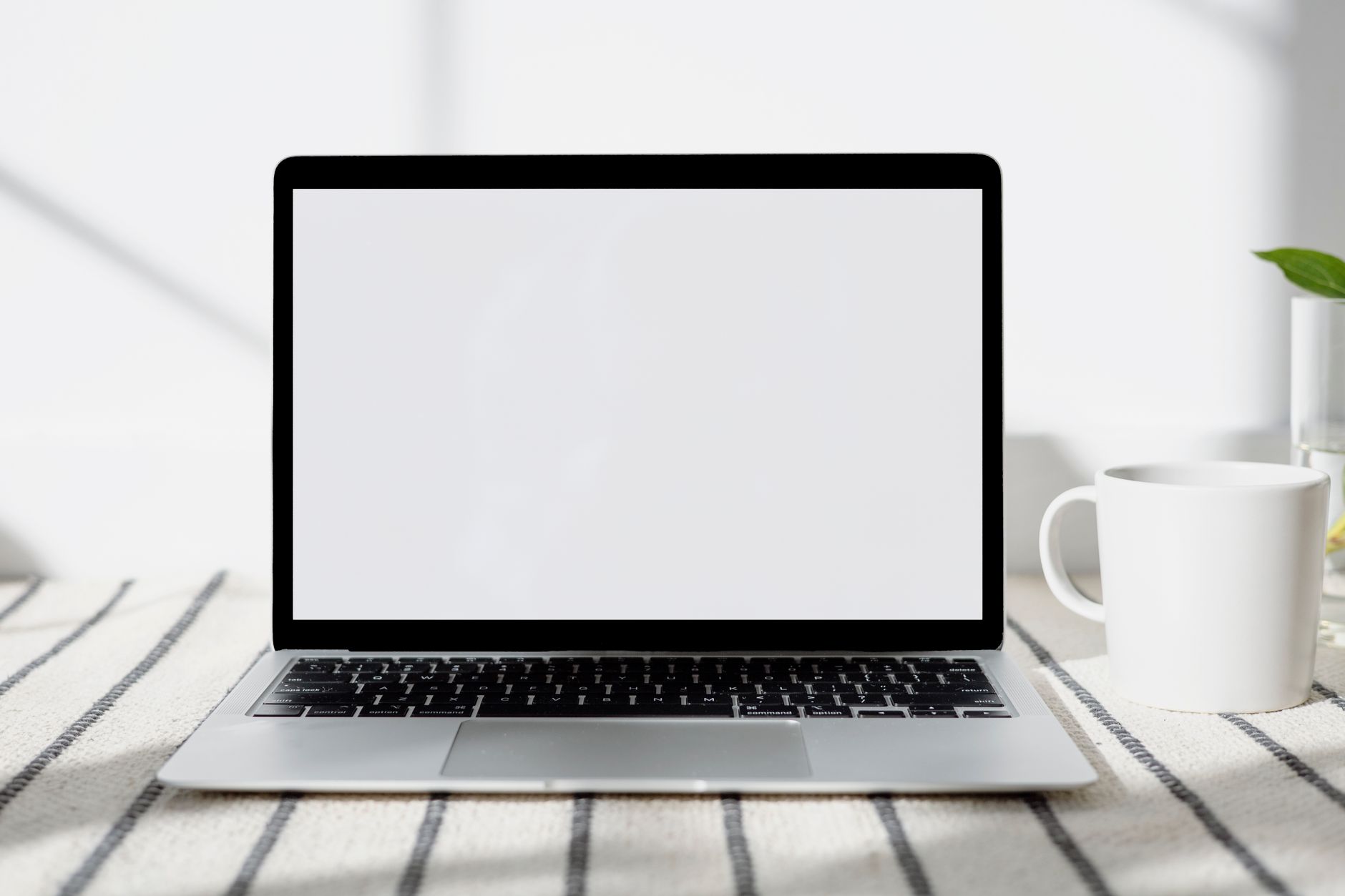 Un espace de travail minimaliste à domicile, avec un ordinateur portable à écran vide et une tasse, éclairé par la lumière naturelle.